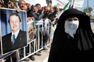 An Algerian woman passes by supporters carrying portraits of President