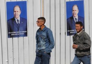 Algerian men walk past electoral posters of President Abdelaziz Bouteflika