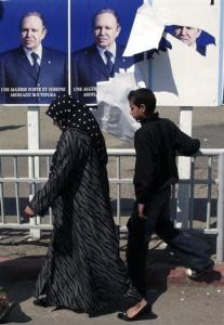 People walk past electoral posters for outgoing president Abdelaziz Bouteflika