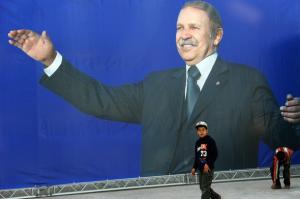Algerian children walk next to a huge electoral poster of