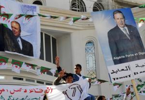 Algerian youths flash the V-sign among posters portraying Algerian President