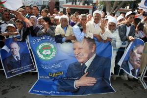 Algerians stand behind posters of President Abdelaziz Bouteflika during an