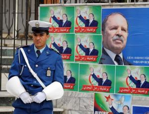 An Algerian policeman stands in front of posters showing President