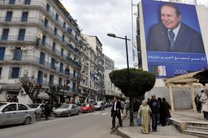 Algerians walk past a banner of Algerian President and presidential