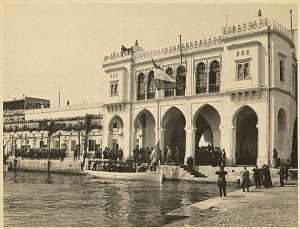 Arrivée de M. Loubet président de la République française. La vue est prise au moment où M. Loubet pose le pied sur la terre algérienne. Sous la voûte se trouvent les autorités algériennes, à gauche la musique des zouaves. L'amirauté ancienne construction (Photo rare)