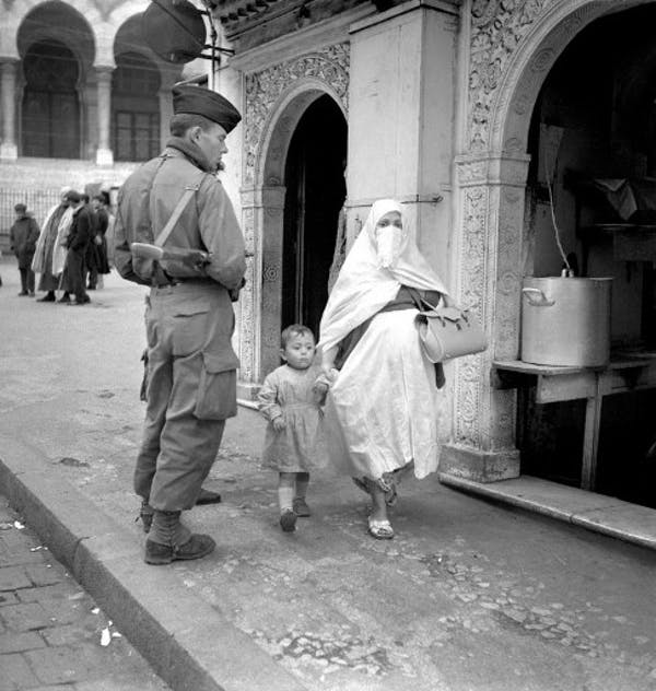 Une femme voilée et son enfant passent dans une rue d’Alger sous le regard d’un soldat français pendant la guerre d’Algérie