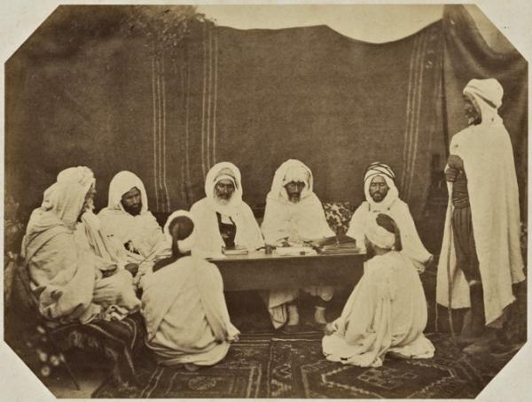 Midjelés de Mostaganem. Si Ahmed Bou Chenin, adel thaleb. Si Mohammed Ould El Bey Brahim bach-adel, thaleb alem. Si Ben Aouda, kadi de Mostaganem. Si Mohammed El Agachi, muphti 'président). Si Mohammed ben Kartaba, cadhi militaire. Si el Khatir, huissier, thaleb alem. Ahmed Bel Gassem sous-huissier, deux plaideurs (Image de propagande coloniale)