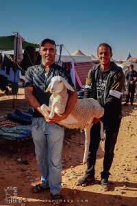 Deux hommes robustes portant un mouton : la solidarité au marché