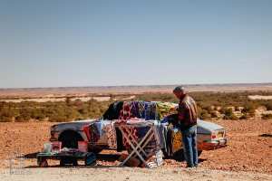 Vendeur de vêtements seul avec sa voiture dans l'immensité du désert : l'isolement et la détermination