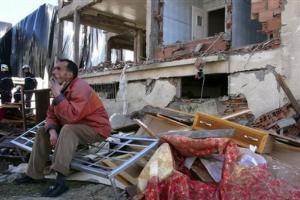 A resident sits by the wreckage of a building,