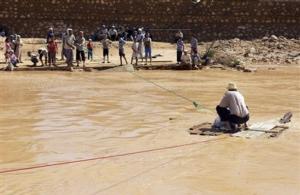 Residents on a river bank pull a man across