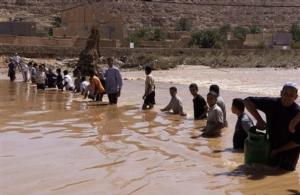 Residents transport gas bottles across a river in the